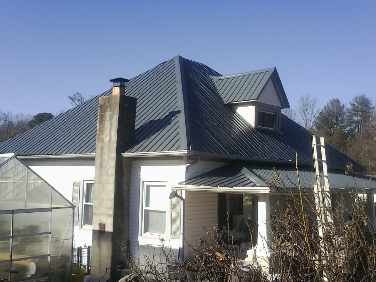 Dark blue standing seam metal roof on a white farmhouse with dormer — Slate & Tile Roof Repair by Roofing Brothers in Craig