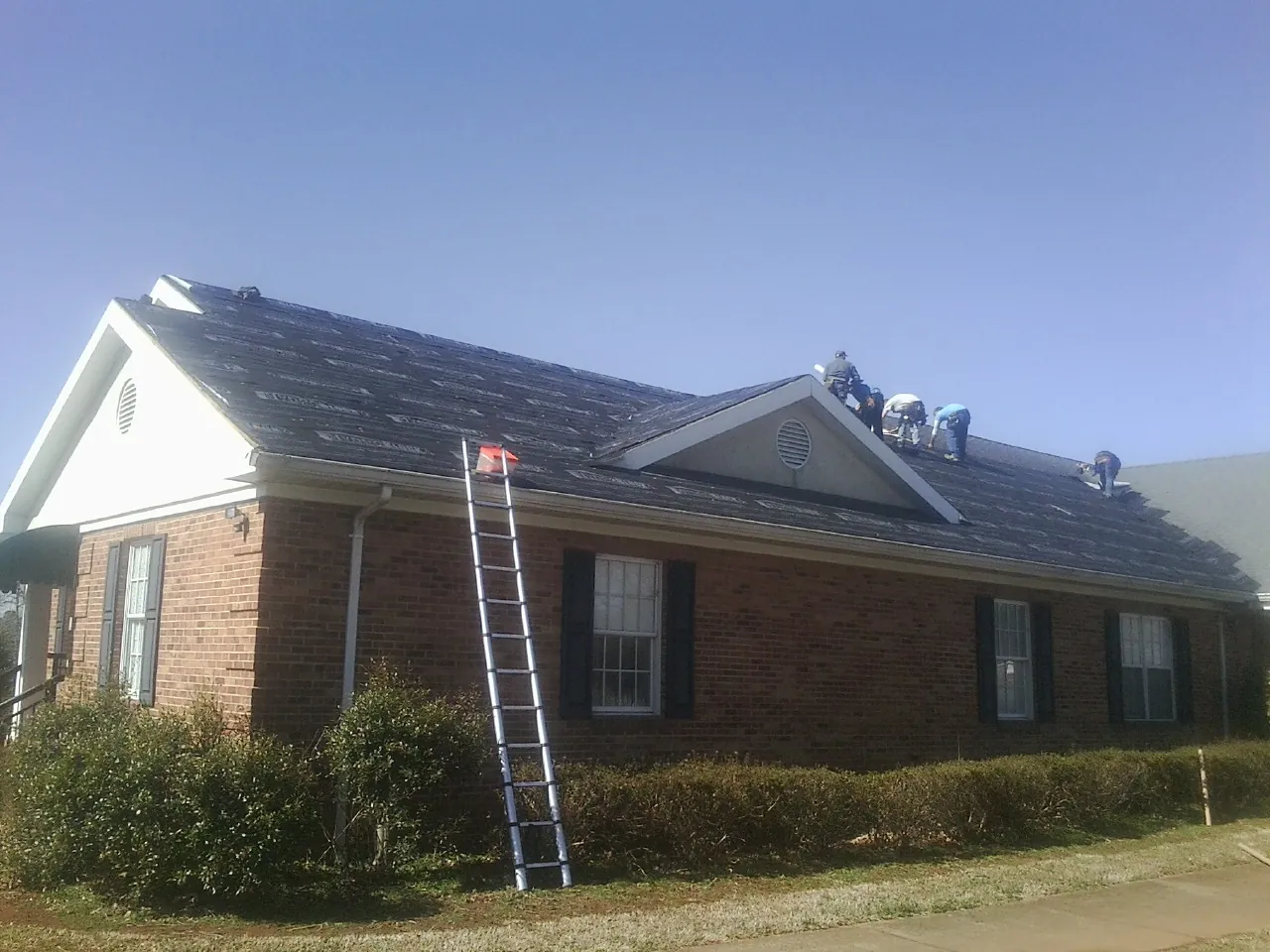 Crew tearing shingles off a brick ranch roof with a ladder set — Metal Roof Repair work by our crew in Craig