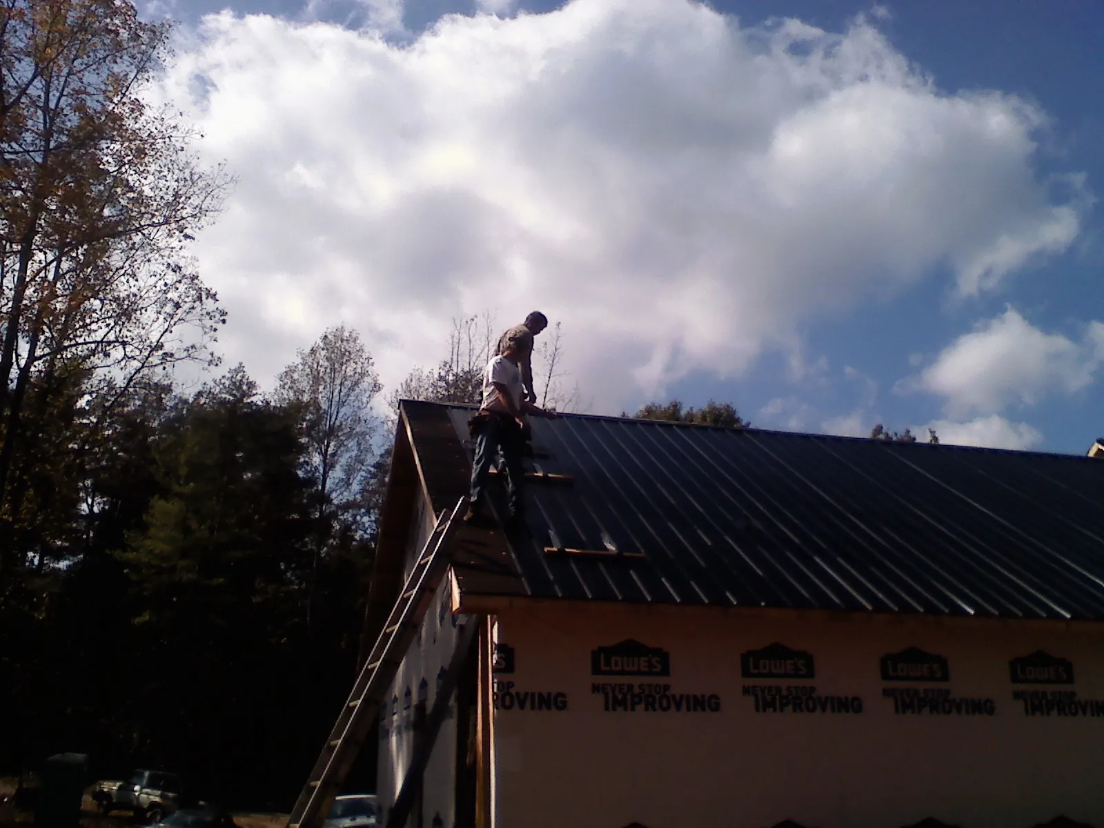 Roofer fastening dark metal panels high against a cloudy sky, from a Roof Inspection job in Craig
